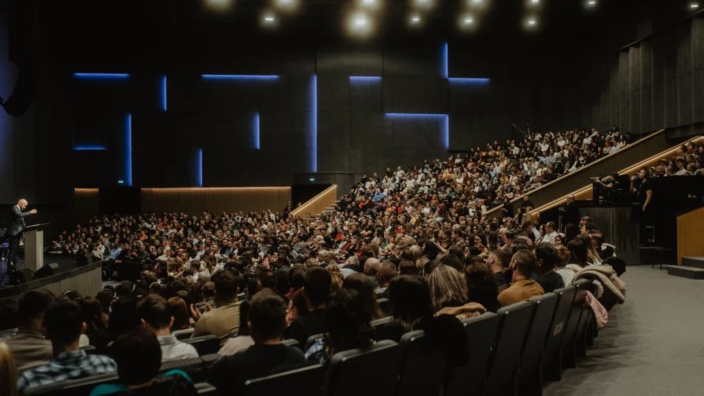 Large audience in a lecture theatre listening to a speaker on stage