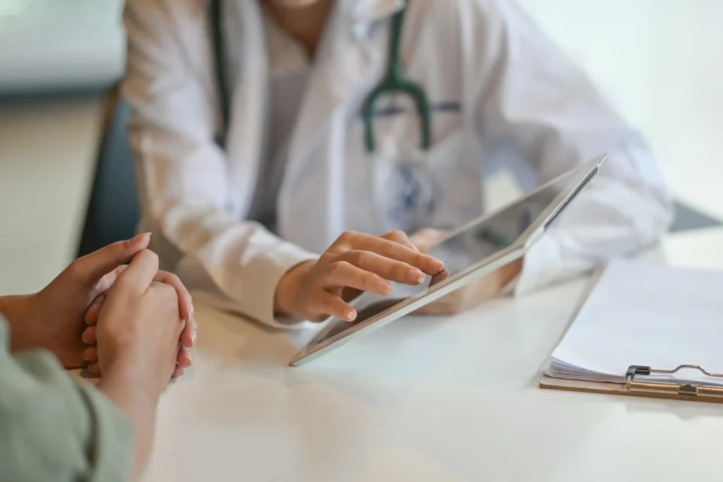 Doctor with a stethoscope reviewing notes on a tablet during a consultation with a patient