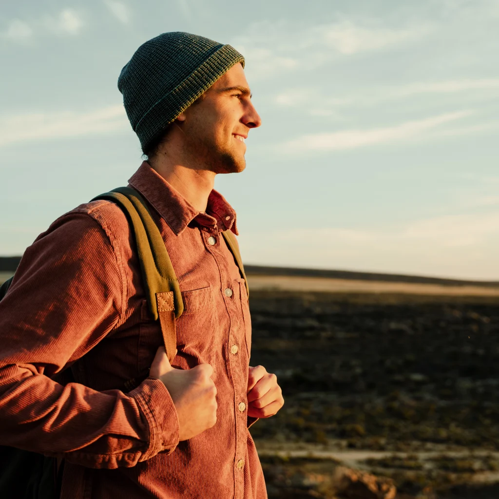 Smiling young man with a backpack walking outdoors at sunset