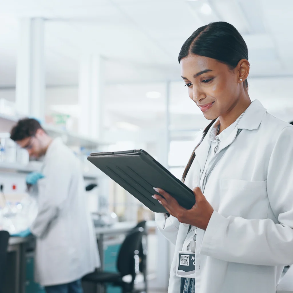 Scientist in a lab coat smiling at a tablet in a laboratory