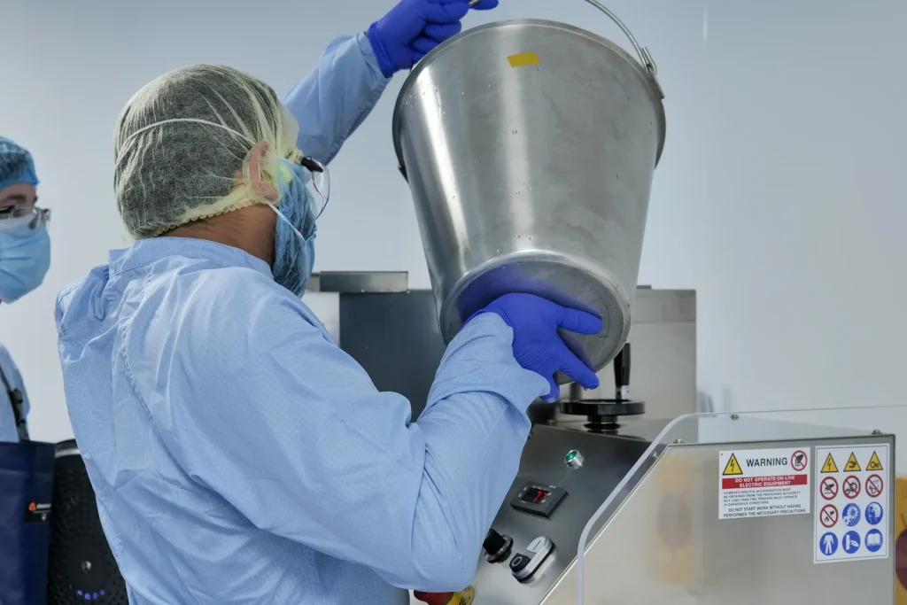 Technician in protective clothing pouring ingredients into a pastille-making machine at the Curaleaf Laboratories site